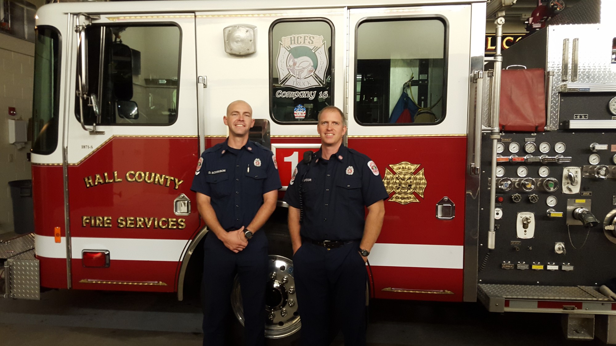 Daniel Morrison and Nathan DeFoor in Hall County Fire Services uniforms, standing in front of a fire engine in the station bay